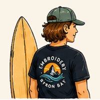 Person wearing an EBB embroidered cap and t-shirt, holding a surfboard